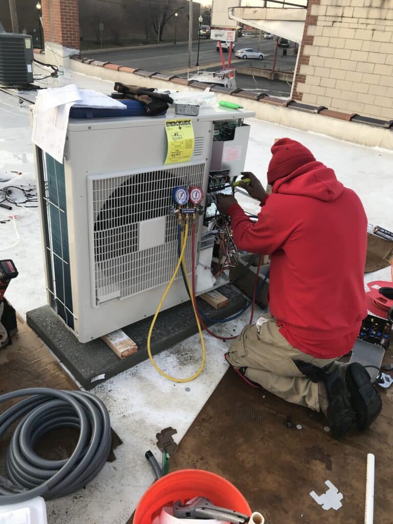 Technician servicing rooftop AC unit with gauges in Florissant, MO.