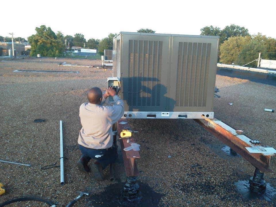 Technician servicing a rooftop HVAC unit on a flat roof in Florissant MO